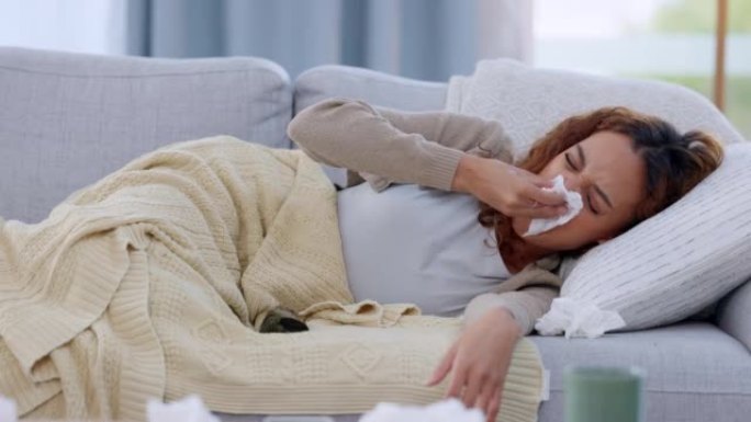 在禁闭期间，生病的女人用纸巾在家里的沙发上用毯子包裹着鼻子。年轻女性感到不适，患有感冒或流感病毒并隔