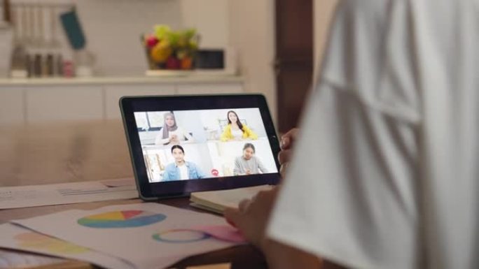 亚洲女商人使用数字平板电脑通过视频通话与同事讨论计划头脑风暴在线会议，同时在家厨房远程工作。