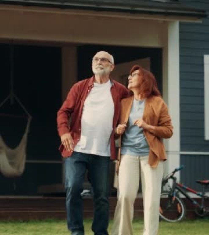 垂直屏幕: 健康的老年夫妇走在他们住宅区的户外，互相拥抱。爱成人，谈心，乐在其中，指向远方，享受他们