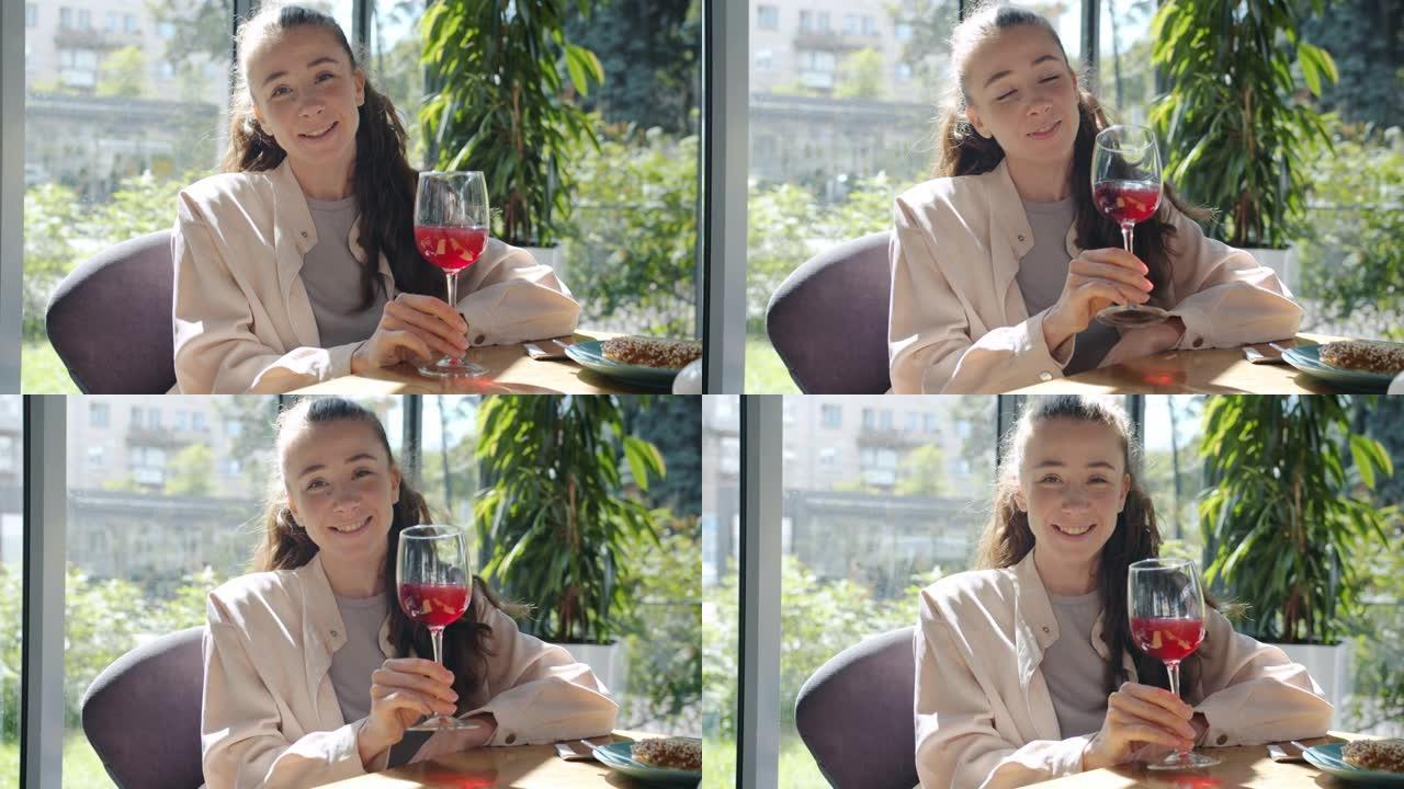 快乐女孩的肖像坐在咖啡馆里独自微笑着看着相机，玩一杯红酒