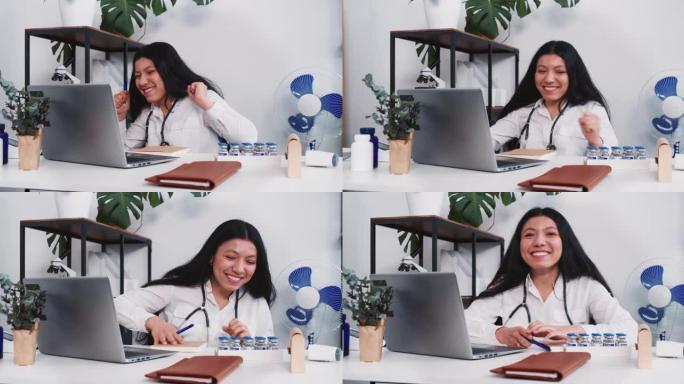 快乐兴奋的多民族女医生微笑着庆祝战胜疾病在办公室桌子上工作笔记本电脑。