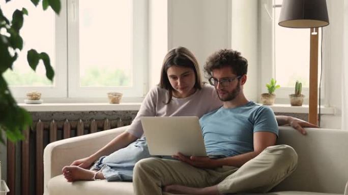 可爱的年轻妻子看着丈夫在笔记本电脑上玩电脑游戏