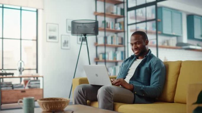 英俊的黑人非洲裔美国男子坐在舒适的客厅的沙发上，在笔记本电脑上工作。自由职业者在家工作。浏览互联网，