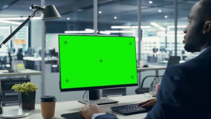 成功的黑人商人坐在办公桌前，在办公室里用绿屏笔记本电脑工作。使用色度键显示的非裔美国商人。肩膀放大