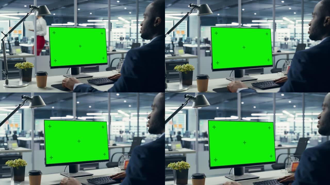 成功的黑人商人坐在办公桌前，在办公室里用绿屏笔记本电脑工作。使用色度键显示的非裔美国商人。肩膀放大
