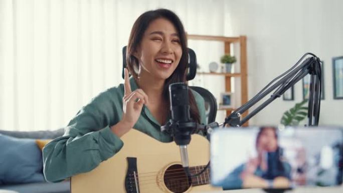 十几岁的亚洲女孩影响者玩吉他音乐使用麦克风记录和智能手机在线观众在家收听。