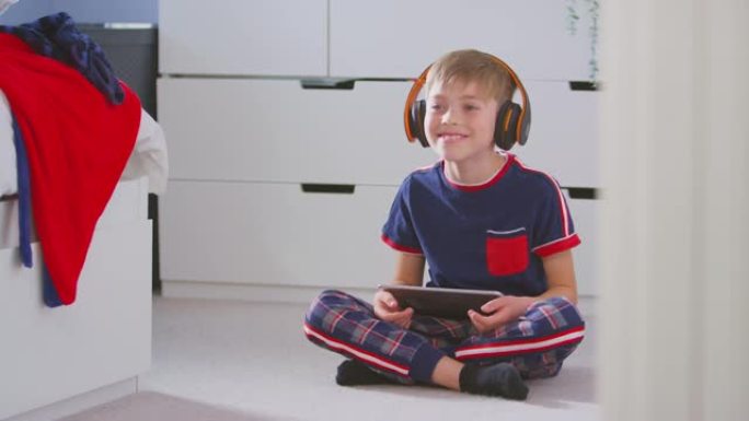 卧室里的男孩戴着无线耳机在数字平板电脑上听音乐