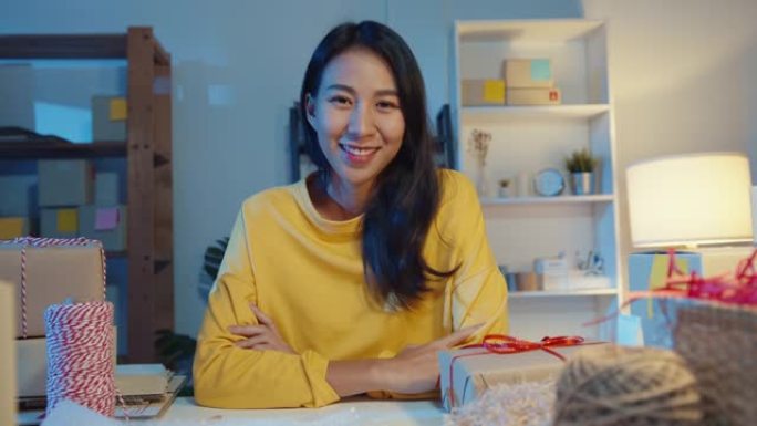 年轻的亚洲女商人的肖像感到幸福的微笑，双臂交叉，晚上在家庭办公室工作时看着相机。