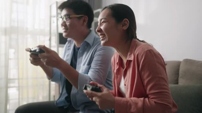 快乐的亚洲夫妇坐在沙发上，在控制台上玩电子游戏