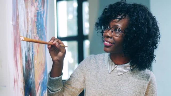 戴着眼镜的非洲族裔女士在用刷子绘画时微笑着