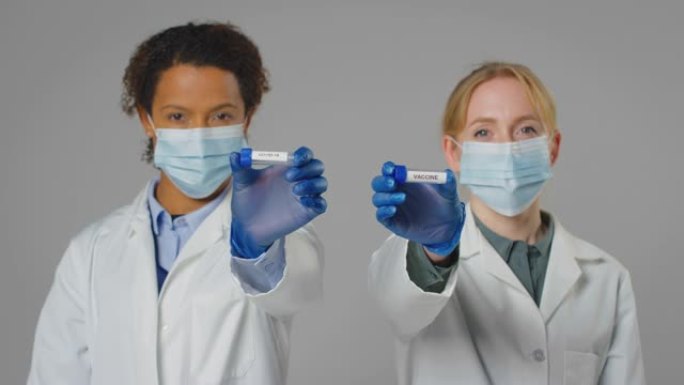 实验室研究人员戴着口罩，手里拿着标有疫苗和Covid-19的试管