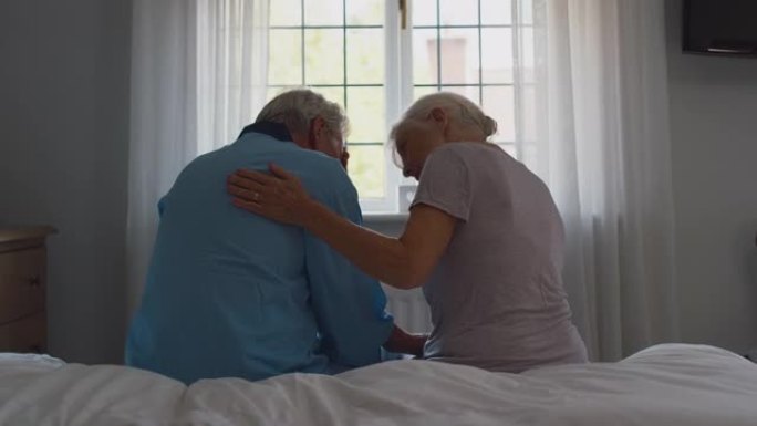 担心的退休高级夫妇坐在家里的床上与女人一起讨论问题，安慰男人慢动作射击