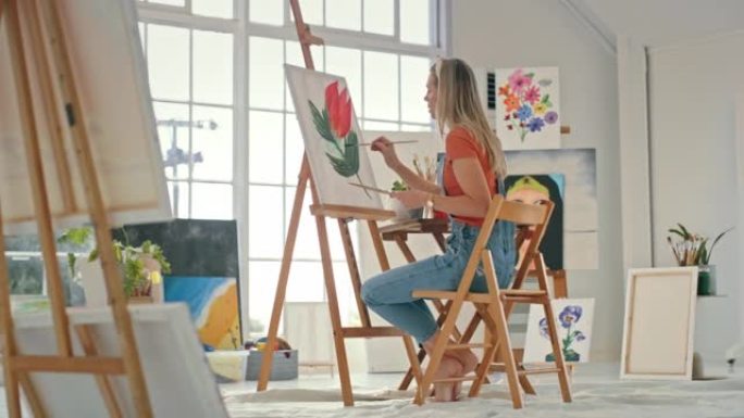 年轻的女画家在工作室里在画布上画彩画。一位严肃的女性在车间用画笔画一朵花。女人在商店画玫瑰的图像