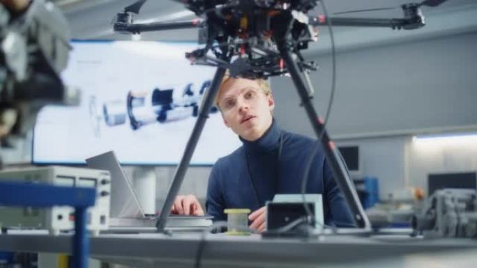 年轻的自动化男工程师的肖像在笔记本电脑上打字，并在工厂的无人机上放主板。现代设备概念与无人机行业的新