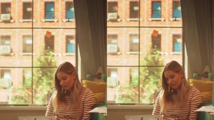 金发女子使用笔记本电脑的垂直视图，而坐在舒适时尚的公寓的客厅地板上。迷人的女孩正在思考和编码