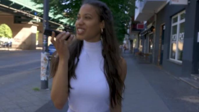 年轻女子在城市里散步时对着智能手机说话