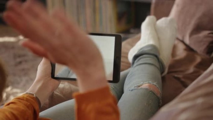 女人使用数字平板电脑手持问候挥舞着朋友坐在家里的沙发