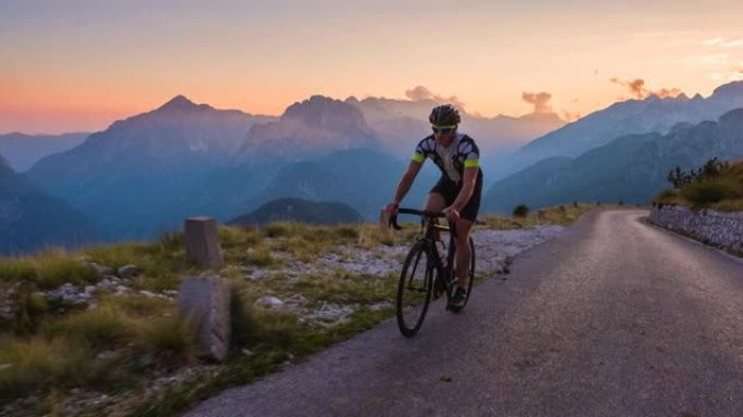 确定的男性公路自行车手在黎明时在山坡上踩踏板