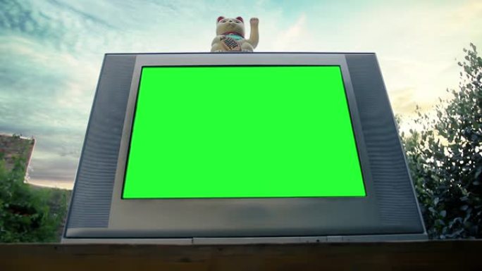 日落时，带有绿色屏幕的复古电视上的Maneki Neko Cat或Fortune Cat。低角度视图