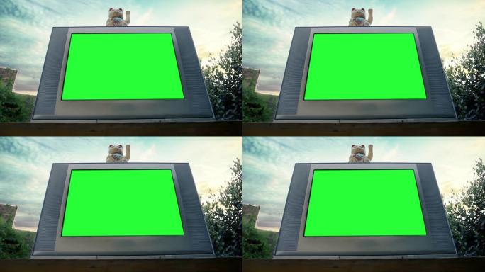 日落时，带有绿色屏幕的复古电视上的Maneki Neko Cat或Fortune Cat。低角度视图