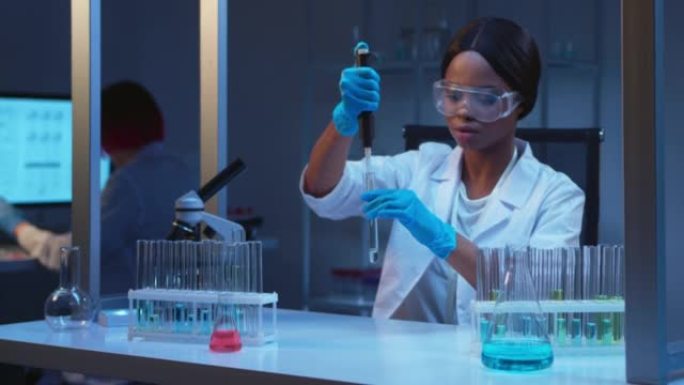 一位年轻的非裔美国女化学家在防护眼镜中工作，在现代实验室中使用玻璃试管和微量移液管