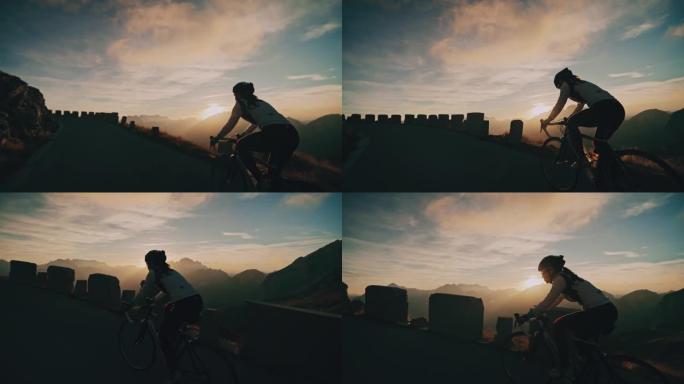 骑自行车的女骑车人在日出山区的公路上坡