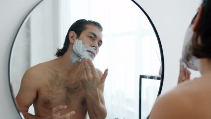 赤裸上身的男人在浴室里用剃须膏看着镜子里的倒影