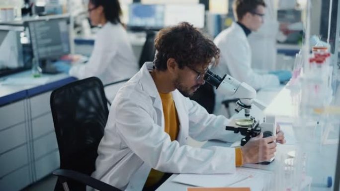 医学科学实验室: 英俊的拉丁科学家在显微镜下观察，写下分析数据。年轻的生物技术专家，使用先进的设备。