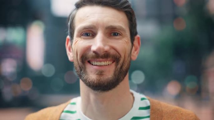 一个穿着便装的快乐英俊的大胡子男人站在街上看着相机，微笑着的肖像。时尚的年轻成年或中年早期有胡须的男