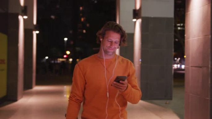 白人男性戴着耳机和滑板，微笑，走路，在街上使用手机