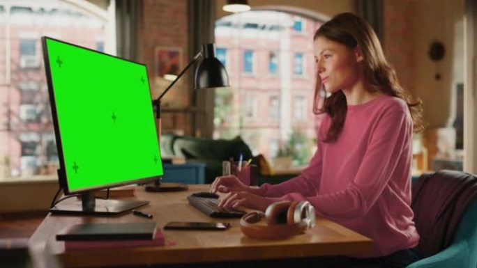 年轻漂亮的女性在家用绿屏模拟显示的台式电脑工作。有创造力的女人检查社交媒体，浏览互联网。阁楼公寓，从