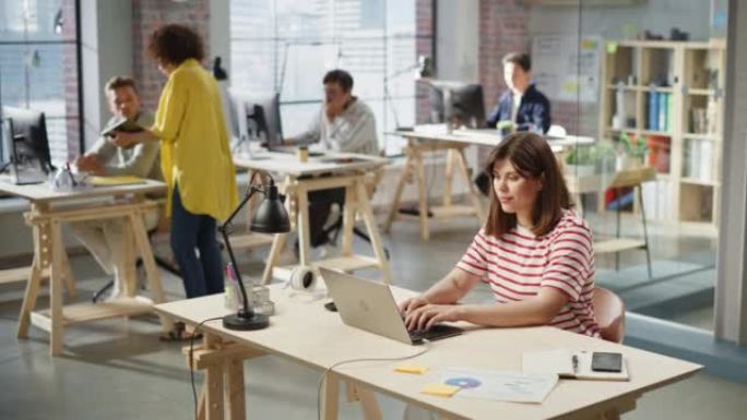 在活跃的当代办公室中使用计算机的多元化创意团队成员。年轻女性媒体关系经理致力于笔记本电脑品牌创新战略