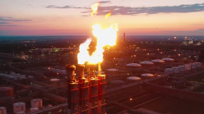 日落时拍摄的炼厂气耀斑和工厂建筑。气候变化概念。