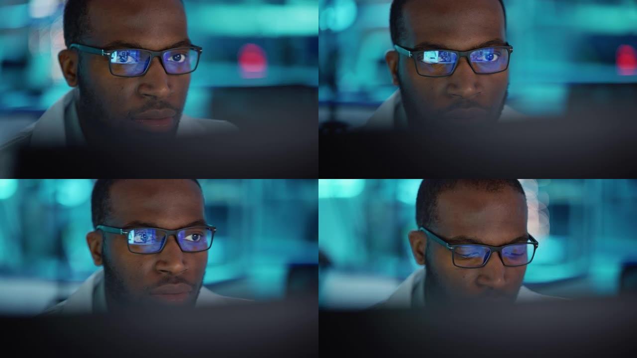 戴着眼镜的英俊黑人男子的肖像自信地在电脑上工作。年轻聪明的男性工程师或在实验室工作的科学家。Boke