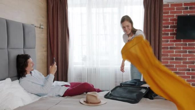 年轻女子在酒店房间与衣服合影，男子用智能手机拍照