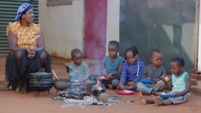 非洲的贫困。饥饿的非洲黑人儿童坐在火炉旁吃玉米/玉米和鸡肉
