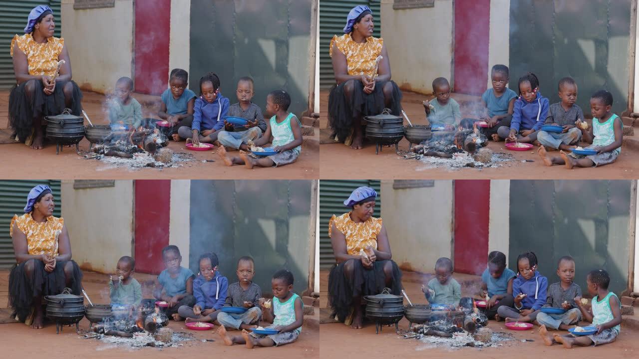 非洲的贫困。饥饿的非洲黑人儿童坐在火炉旁吃玉米/玉米和鸡肉