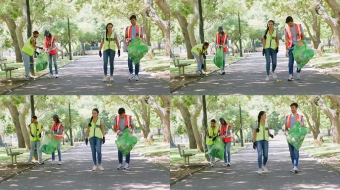 年轻的志愿者在公园里一起捡垃圾。一群人背着袋子在外面的植物园里收集垃圾。多样化的垃圾收集者在操场上进