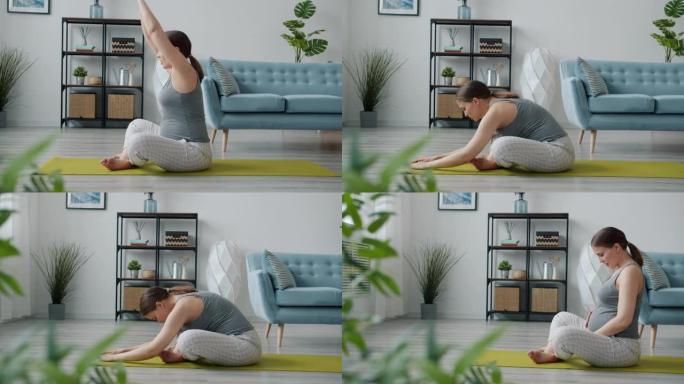 活跃的未来母亲享受瑜伽在垫子上伸展身体，然后放松触摸腹部