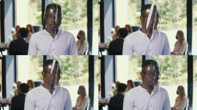 年轻严肃的20多岁非洲办公室经理男子戴着塑料面罩的肖像在轻工作场所慢动作点点头