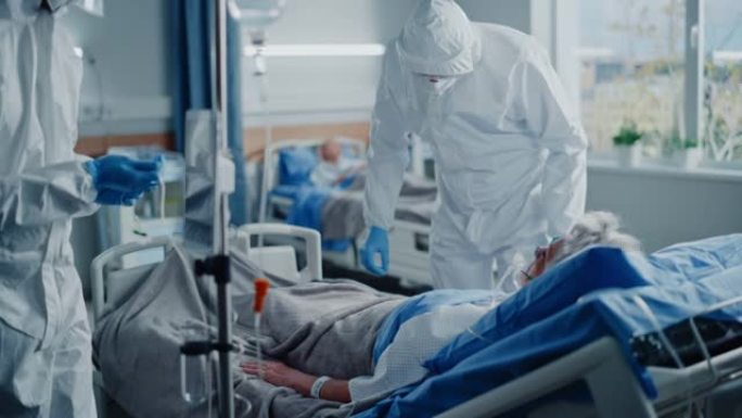 医院冠状病毒急诊科病房: 一队医生穿着工作服，护面罩照顾一名躺在床上的高龄患者，戴上氧气面罩和肺呼吸