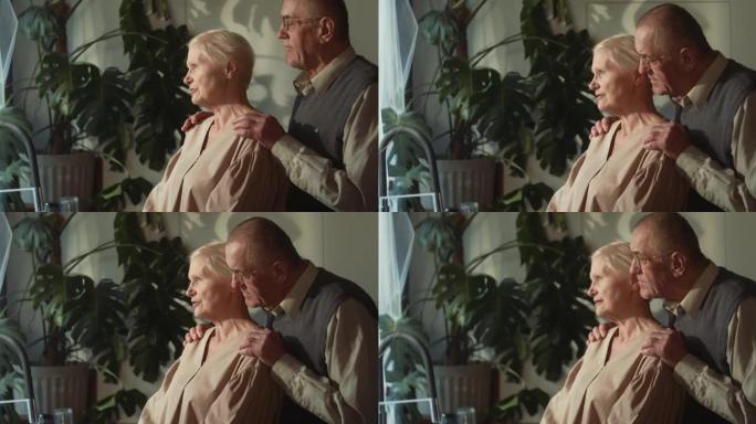 支持和理解。快乐可爱的退休70年代高级丈夫拥抱妻子，在家倾听和微笑。