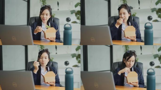 亚洲妇女在笔记本电脑上工作，并在办公室的办公桌工作场所吃沙拉餐