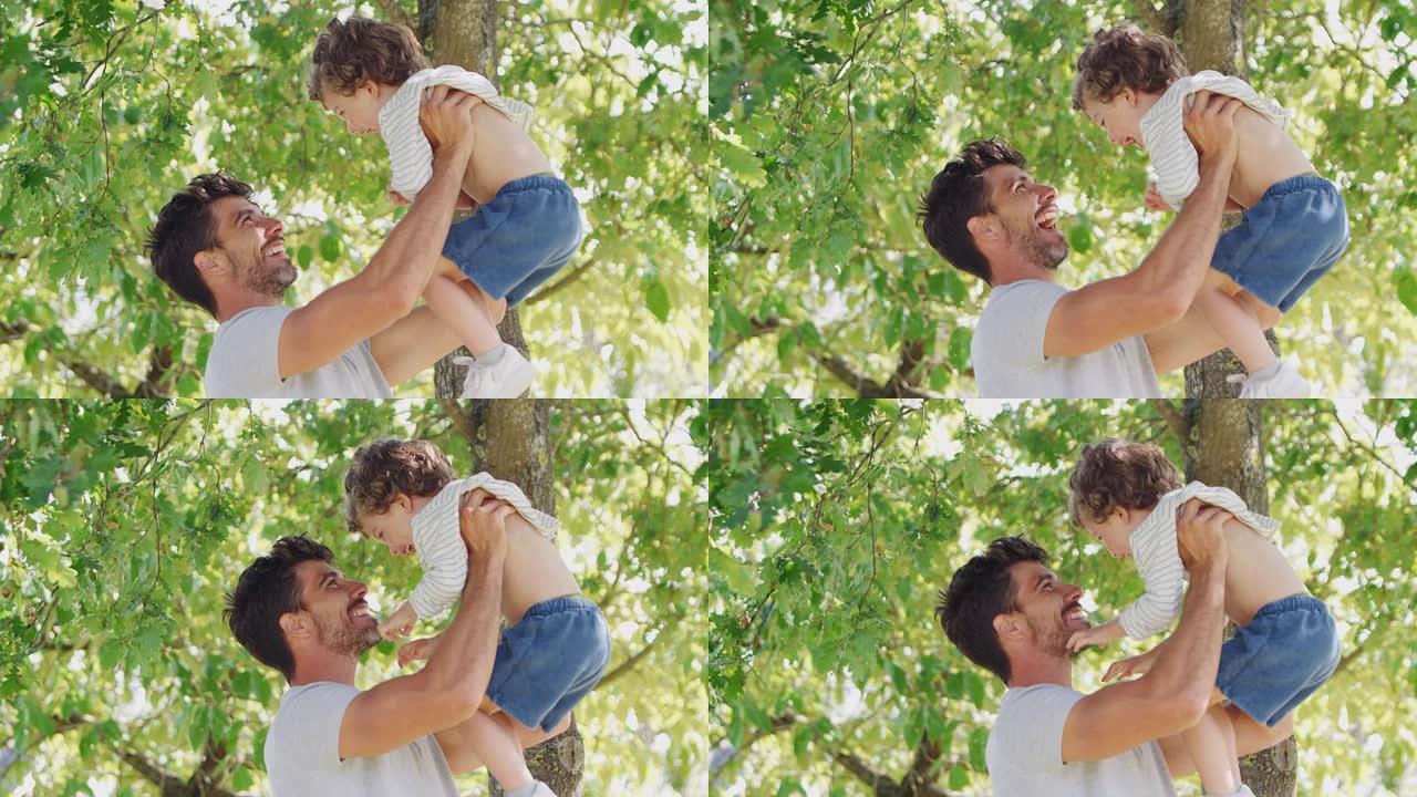 慈爱的父亲和儿子在公园里玩得开心，在绿树成荫的背景下将他抱在空中