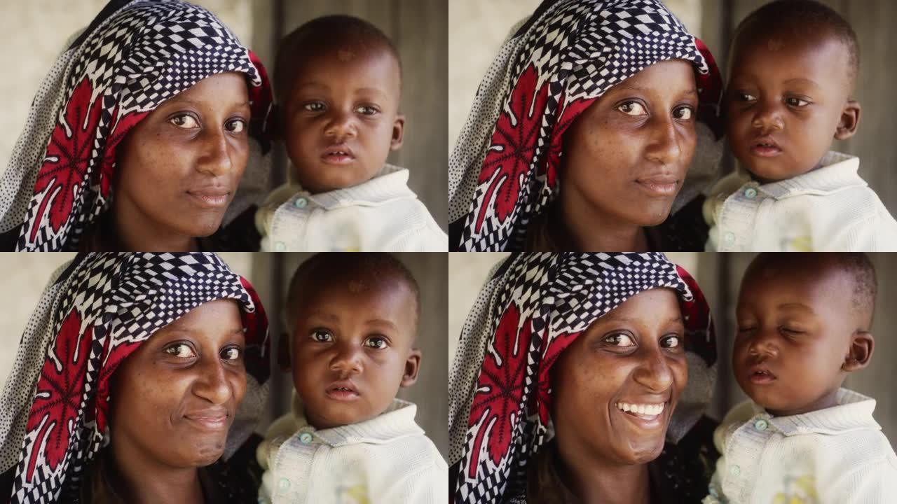 一位穿着传统服装的美丽的非洲年轻母亲的肖像认真地看着相机，然后微笑着将她的蹒跚学步的孩子抱在怀里。年