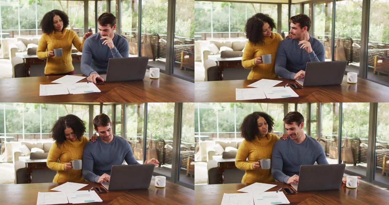 幸福的多元化夫妇在客厅聊天，使用笔记本电脑，看文书工作并支付账单