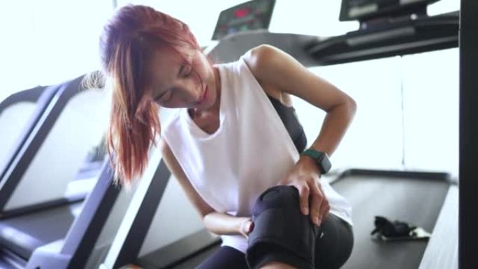 亚洲女子在健身房抱着受伤的膝盖，4k手持中拍实时