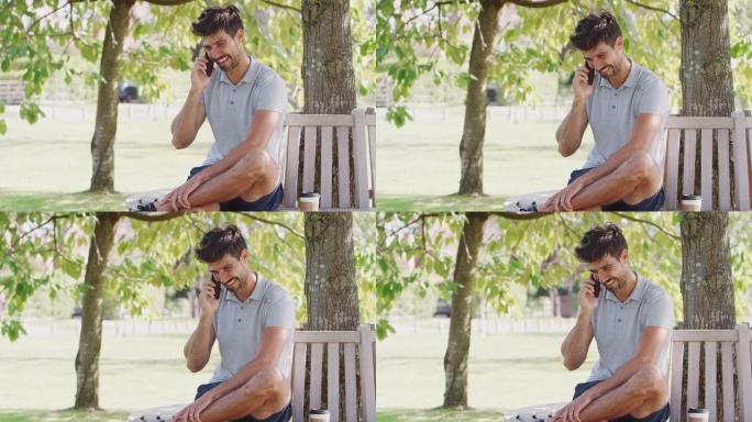 男子穿着夏季短裤坐在公园长椅上树下聊天手机