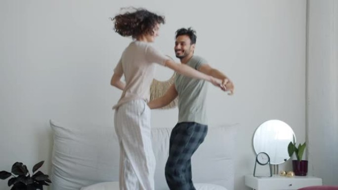 穿着睡衣的阿拉伯男人和高加索女人的慢动作在家里的床上跳舞和大笑