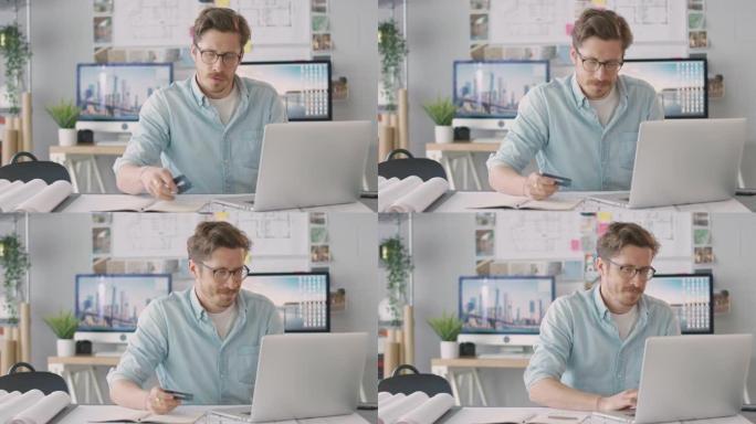 办公室的男建筑师在办公桌前工作，使用笔记本电脑上的信用卡在线购买